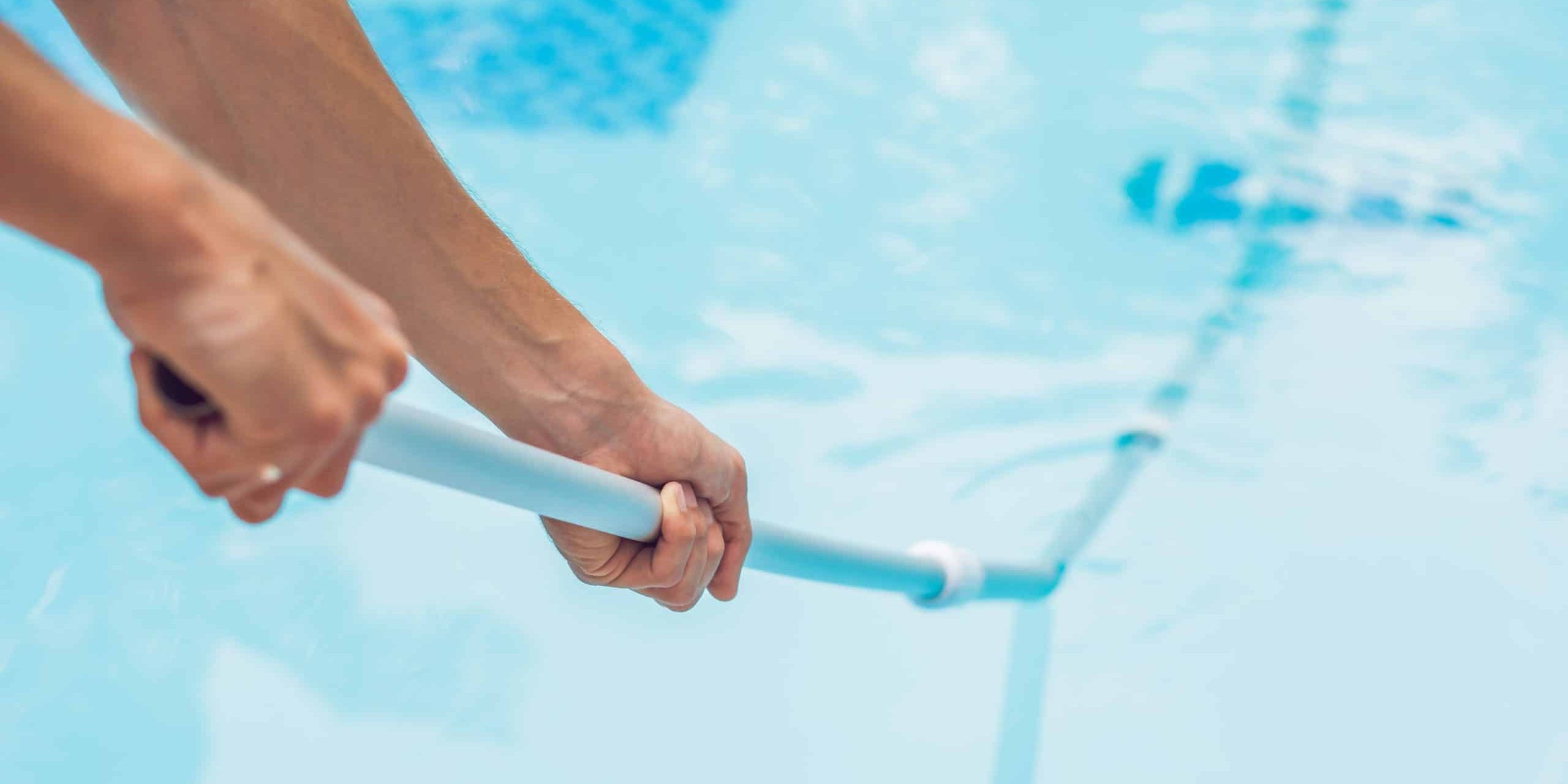 Cleaner of the swimming pool . Man in a blue shirt with cleaning equipment for swimming pools, sunny swimming pool cleaning