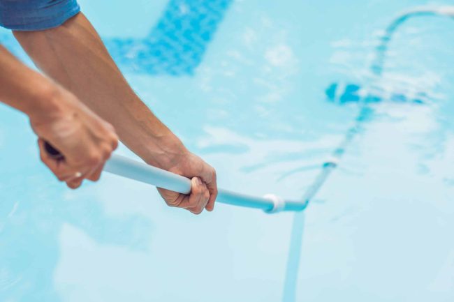 Cleaner of the swimming pool . Man in a blue shirt with cleaning equipment for swimming pools, sunny swimming pool cleaning