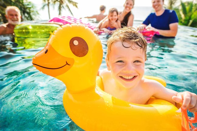 Boy swimming in a pool with family boy floating in a yellow duck