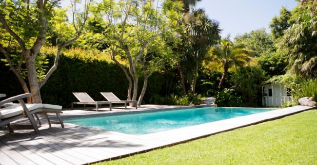 A wide, in-ground pool that has a deck built around the perimeter. There are several lawn chairs on the deck.
