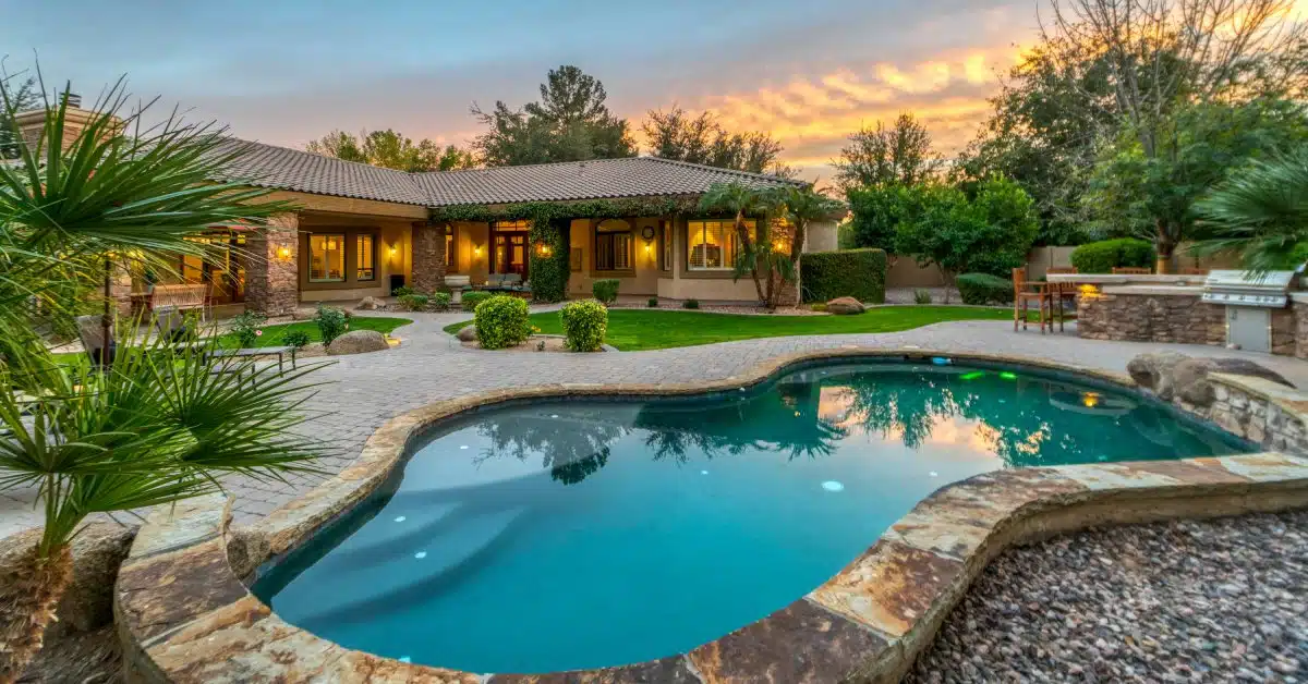 A stunning pool with a wavy, irregular shape surrounded by stones in a beautifully landscaped backyard of a home.