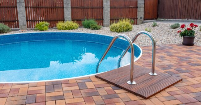 Closeup of a small circular plunge pool surrounded by tile and stones with well-manicured landscaping and a fence.