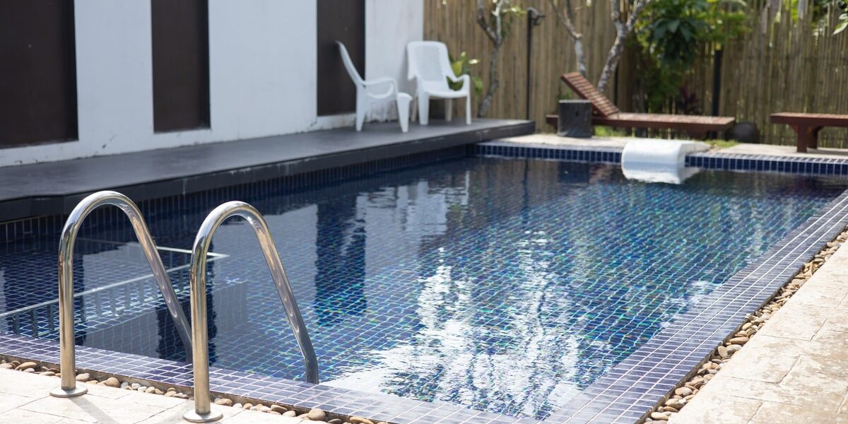 Closeup with a small cocktail pool with a blue tile interior surrounded by pebbles and concrete in a backyard. Closeup with a small cocktail pool with a blue tile interior surrounded by pebbles and concrete in a backyard.