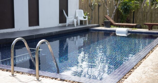 Closeup with a small cocktail pool with a blue tile interior surrounded by pebbles and concrete in a backyard.