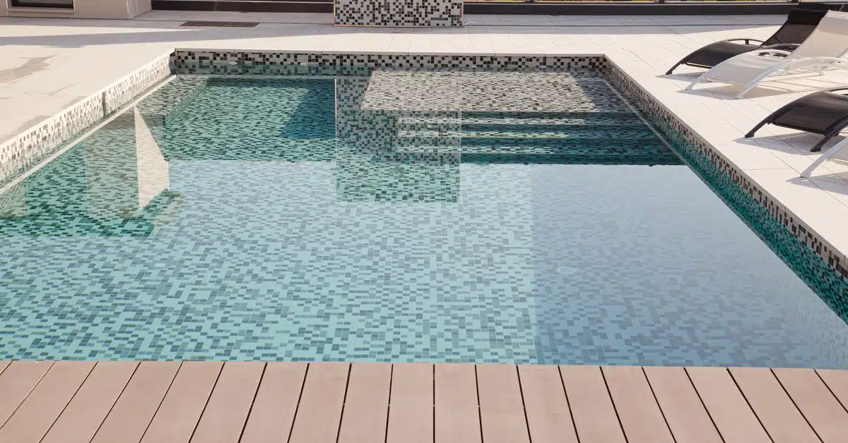 Closeup of a small rectangular cocktail pool with a blue tile interior surface surrounded by concrete in a backyard.