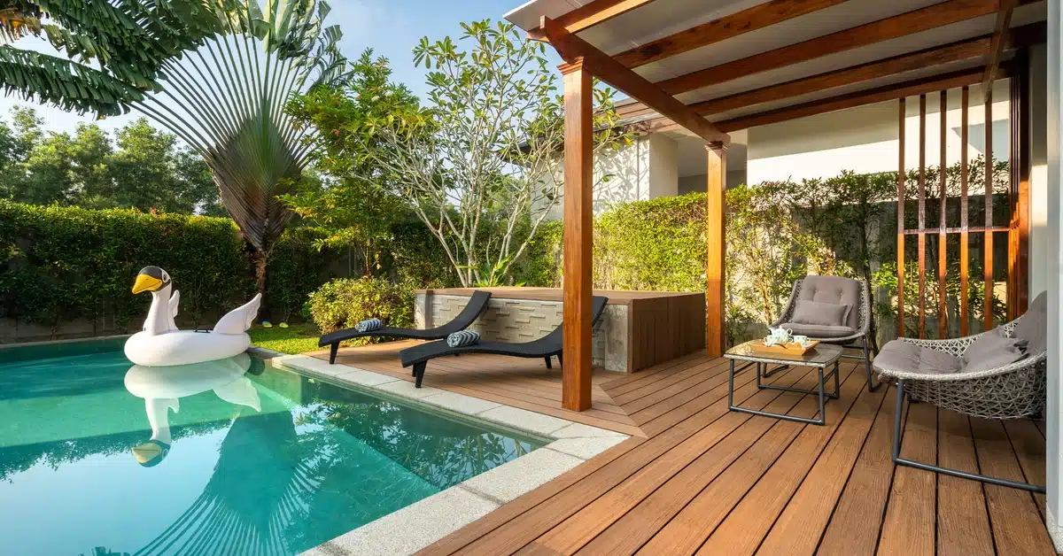 A duck-shaped inflatable tube floating in a pool with a wood deck and two black lounge chairs with striped towels.
