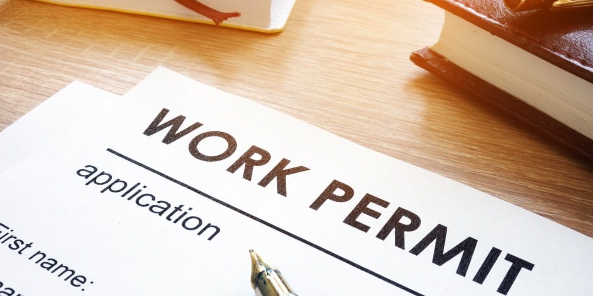 A close-up of a work permit application form on a desk with a pen, books, and leather notebook in warm lighting.