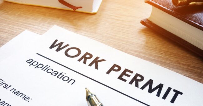 A close-up of a work permit application form on a desk with a pen, books, and leather notebook in warm lighting.